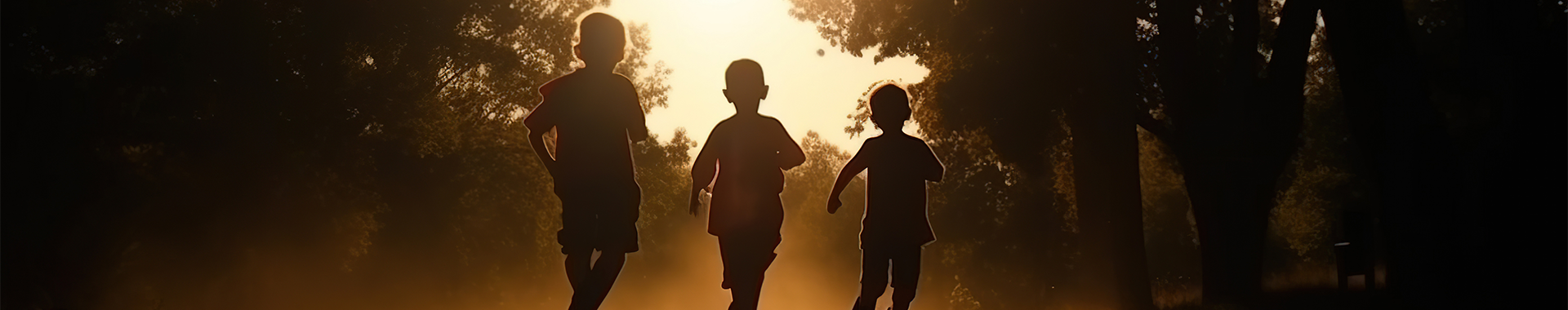 A backlit panoramic view of three children's silhouettes against a sunlit backdrop, capturing a serene moment in a forested park at dusk, conveying a sense of peace and innocence.